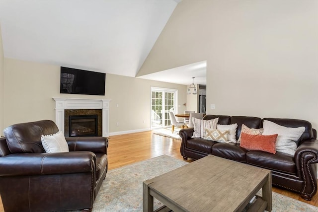 living room featuring high vaulted ceiling, a premium fireplace, light wood-style flooring, and baseboards