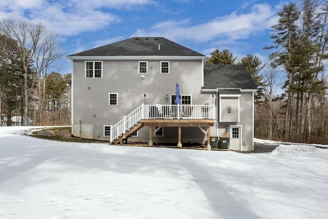 snow covered back of property with stairs, a deck, and roof with shingles