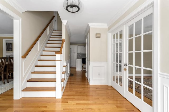 stairway featuring ornamental molding, french doors, wainscoting, and wood finished floors