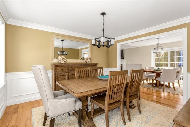 dining room featuring ornamental molding, light wood-type flooring, wainscoting, and an inviting chandelier