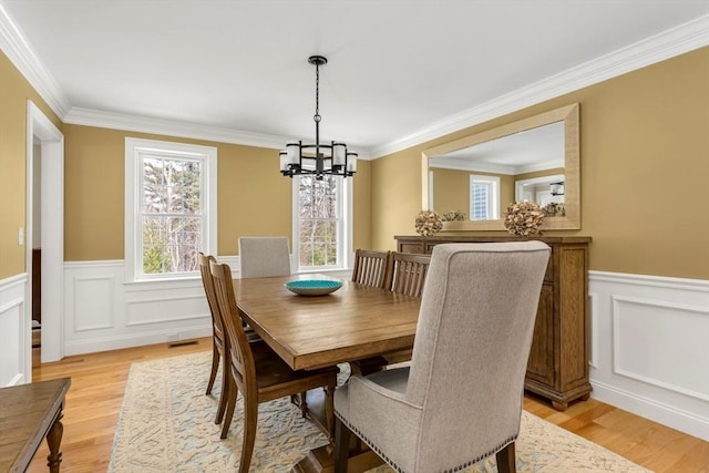 dining area featuring visible vents, a wainscoted wall, crown molding, light wood-style floors, and a chandelier