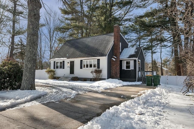 cape cod house featuring a shingled roof, fence, and a chimney