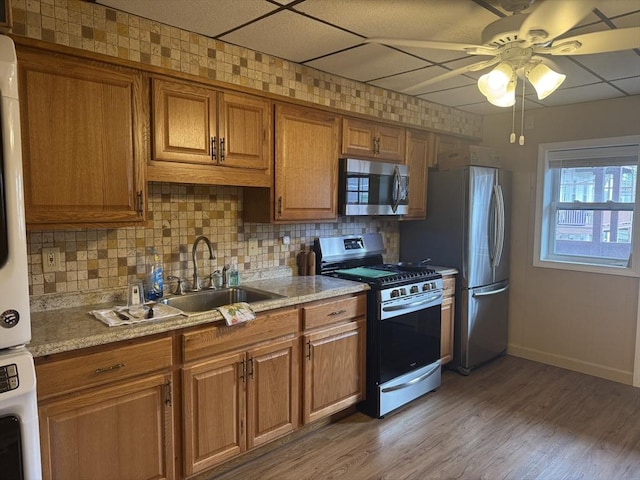 kitchen featuring a sink, brown cabinets, ceiling fan, stacked washing maching and dryer, and appliances with stainless steel finishes