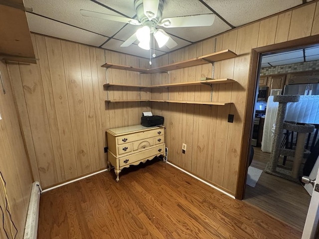 interior space featuring dark wood-type flooring, wooden walls, a baseboard heating unit, and ceiling fan