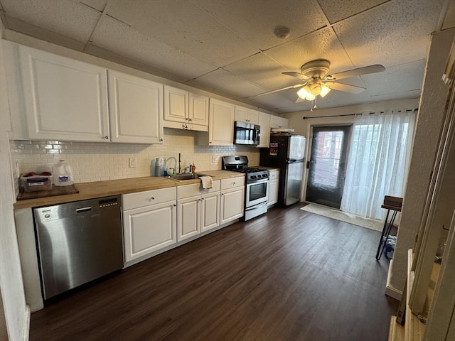 kitchen featuring a sink, a drop ceiling, stainless steel appliances, white cabinets, and dark wood-style flooring