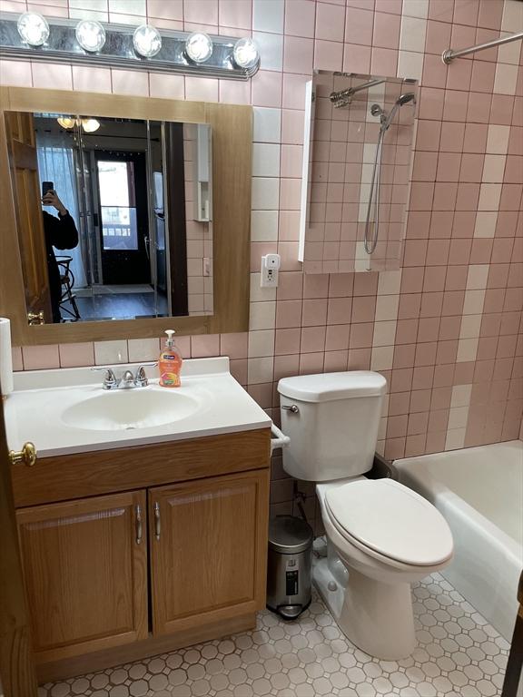 full bathroom featuring vanity, tile patterned floors, tiled shower / bath combo, toilet, and tile walls