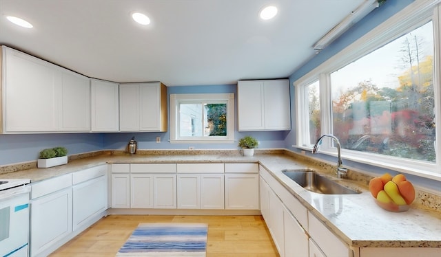 kitchen with light stone countertops, sink, white cabinetry, white stove, and light hardwood / wood-style flooring