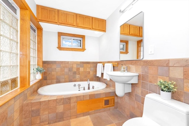 bathroom featuring a relaxing tiled tub, tile patterned flooring, tile walls, and toilet