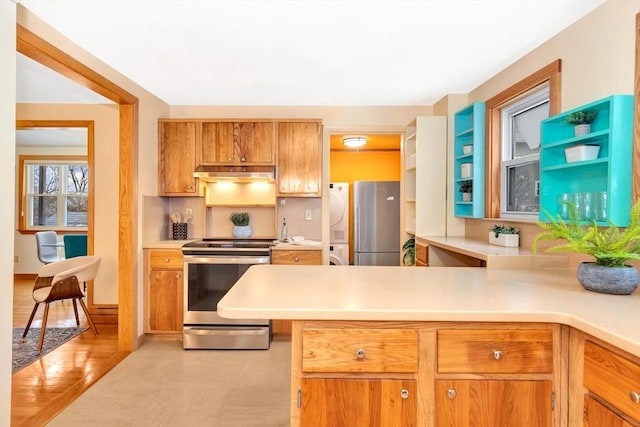 kitchen featuring stainless steel appliances, kitchen peninsula, and stacked washer / drying machine