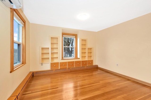 unfurnished living room featuring light hardwood / wood-style flooring, plenty of natural light, a wall unit AC, and baseboard heating