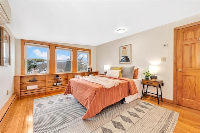 bedroom with a baseboard radiator, hardwood / wood-style floors, and a wall unit AC