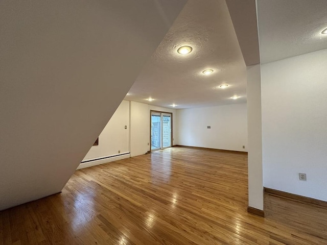 additional living space with baseboards, a textured ceiling, a baseboard heating unit, and wood finished floors