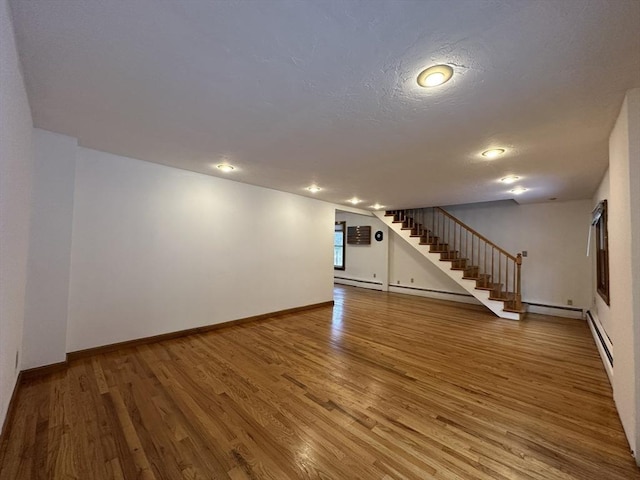 below grade area with a textured ceiling, wood finished floors, baseboards, stairway, and baseboard heating