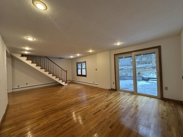 unfurnished living room featuring a baseboard heating unit, wood finished floors, baseboards, and stairs