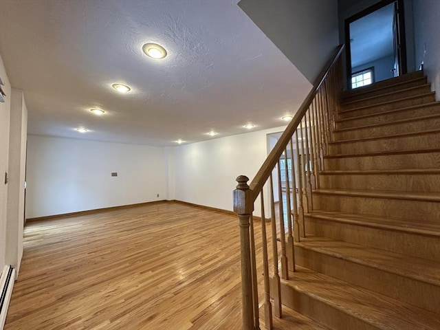 basement with a textured ceiling, a baseboard heating unit, wood finished floors, baseboards, and stairs