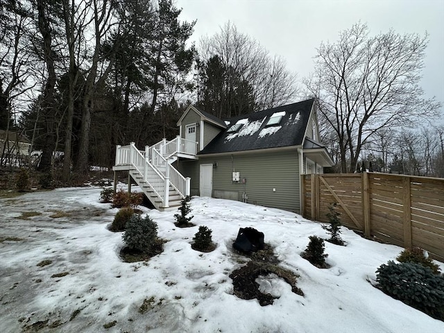 snow covered property with a garage, fence, a shingled roof, and stairs