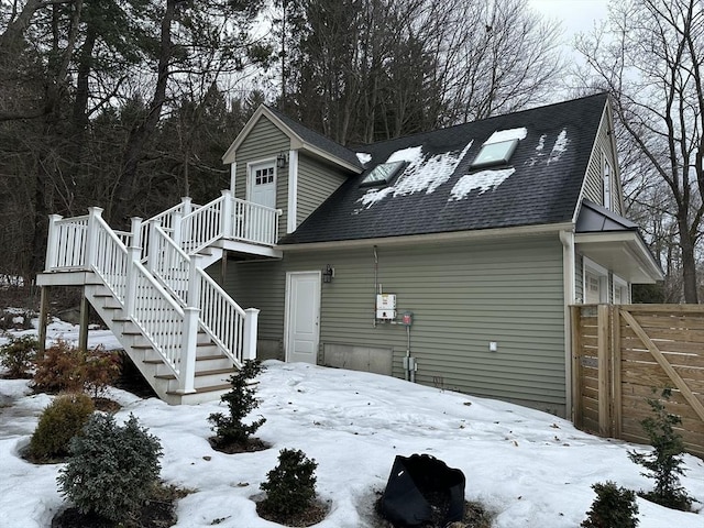 snow covered house featuring a shingled roof, stairway, and a deck