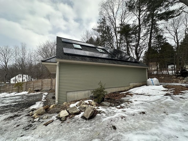 view of snow covered exterior with fence, solar panels, and roof with shingles