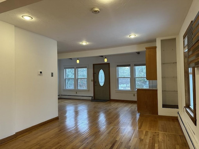 foyer entrance featuring a baseboard radiator, wood finished floors, and a healthy amount of sunlight