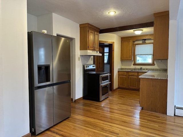 kitchen featuring brown cabinets, stainless steel appliances, a textured ceiling, light wood-type flooring, and under cabinet range hood