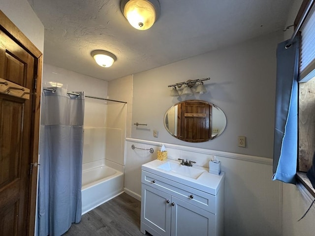 full bath with a wainscoted wall, shower / tub combo, vanity, a textured ceiling, and wood finished floors