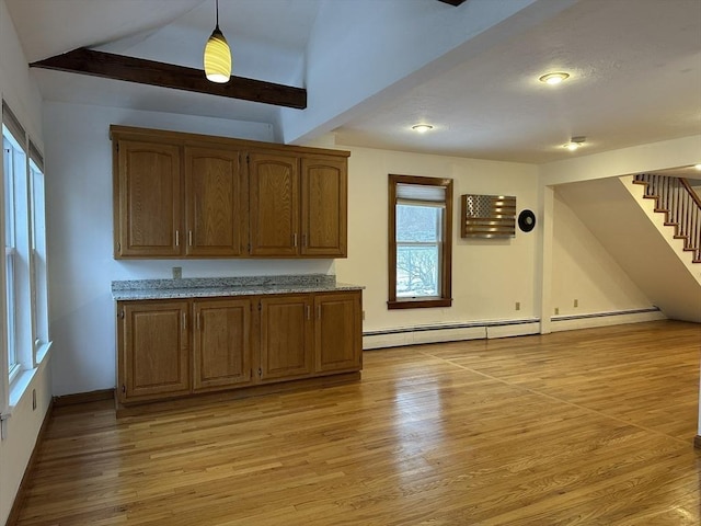 kitchen with pendant lighting, light wood finished floors, lofted ceiling, brown cabinetry, and light stone countertops