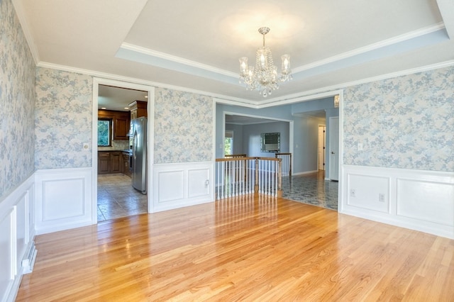 unfurnished room with a raised ceiling, ornamental molding, wood-type flooring, and an inviting chandelier