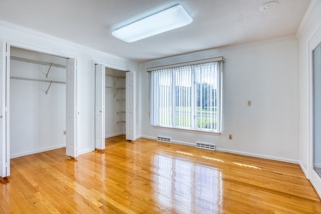 unfurnished bedroom featuring multiple closets, light hardwood / wood-style flooring, a textured ceiling, and ornamental molding