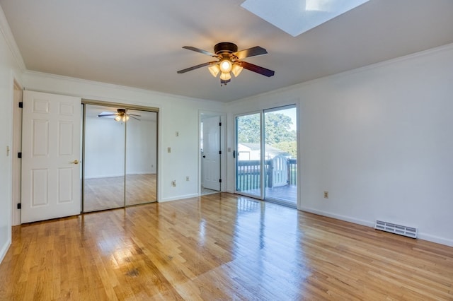 unfurnished bedroom featuring a skylight, ornamental molding, ceiling fan, light hardwood / wood-style floors, and a closet