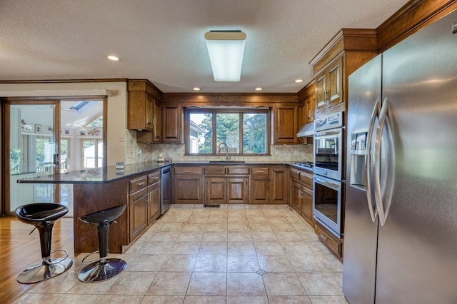 kitchen with kitchen peninsula, a kitchen breakfast bar, tasteful backsplash, stainless steel appliances, and sink