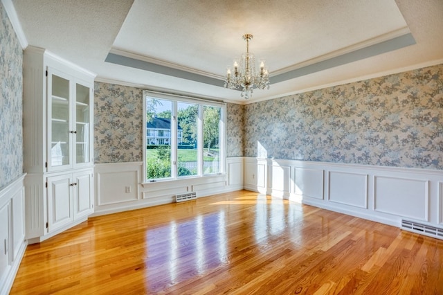 spare room featuring light wood-type flooring, a tray ceiling, and an inviting chandelier