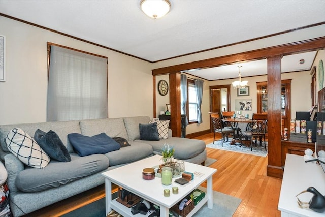 living area featuring light wood-style flooring, ornamental molding, a chandelier, and decorative columns