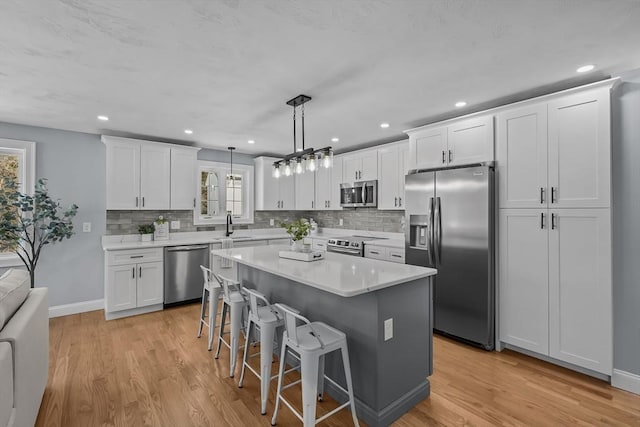 kitchen featuring appliances with stainless steel finishes, a kitchen bar, a center island, decorative light fixtures, and white cabinets