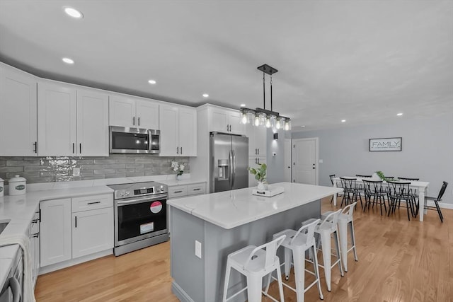 kitchen with appliances with stainless steel finishes, light hardwood / wood-style flooring, decorative light fixtures, a center island, and white cabinetry