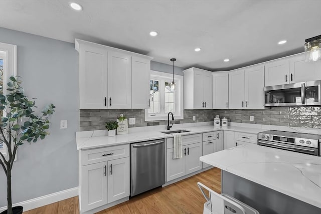 kitchen with stainless steel appliances, white cabinets, decorative light fixtures, light hardwood / wood-style floors, and sink