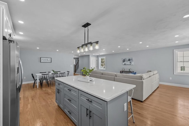 kitchen with gray cabinetry, decorative light fixtures, light hardwood / wood-style floors, stainless steel fridge, and a kitchen island