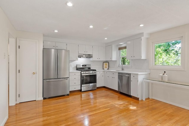 kitchen with stainless steel appliances, under cabinet range hood, light countertops, light wood-style floors, and recessed lighting