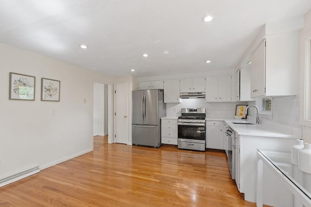 kitchen with stainless steel appliances, under cabinet range hood, a sink, light countertops, and light wood-type flooring