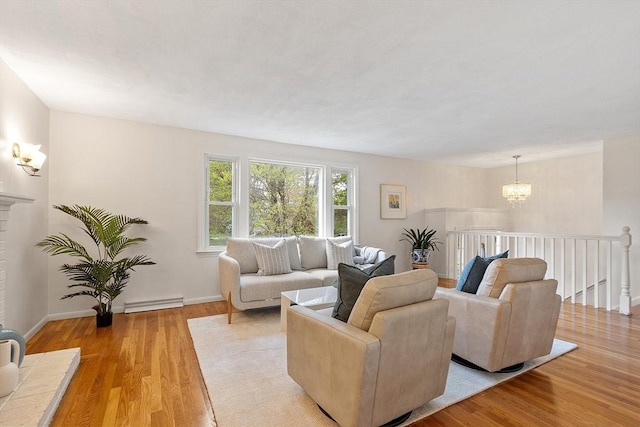 living area featuring light wood-type flooring, a baseboard heating unit, a chandelier, and baseboards