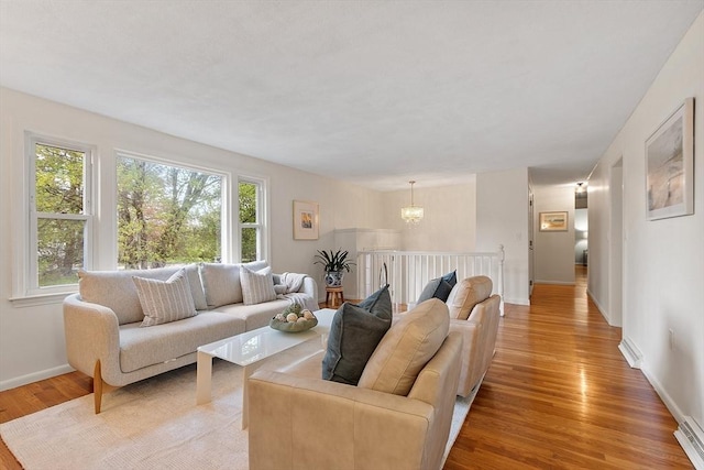 living room with light wood finished floors, a chandelier, and baseboards