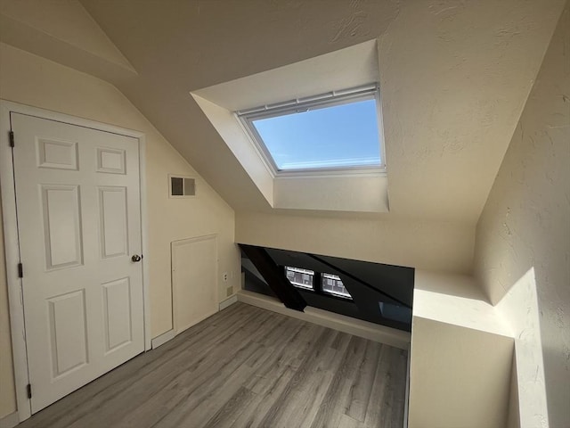 additional living space featuring visible vents, wood finished floors, and vaulted ceiling with skylight
