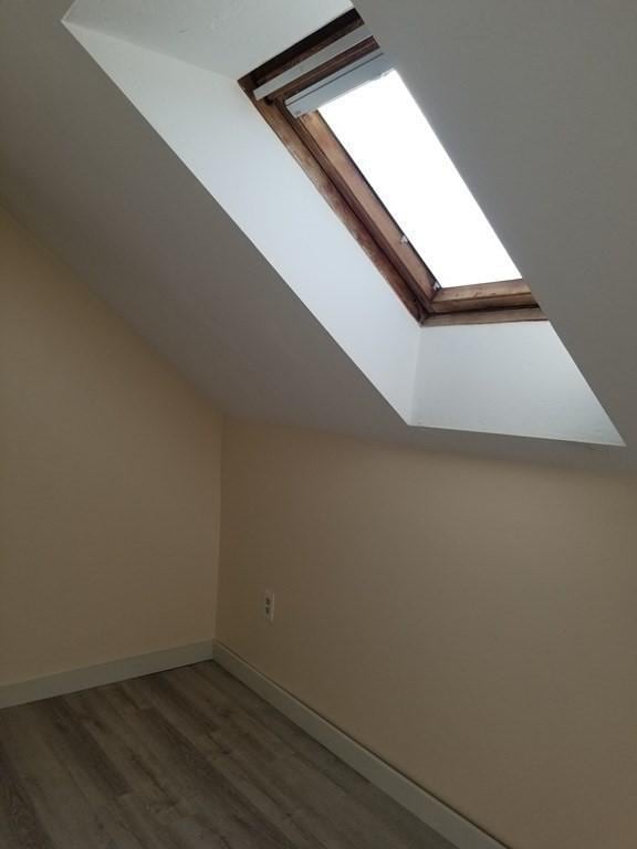 bonus room featuring baseboards, wood finished floors, and vaulted ceiling with skylight