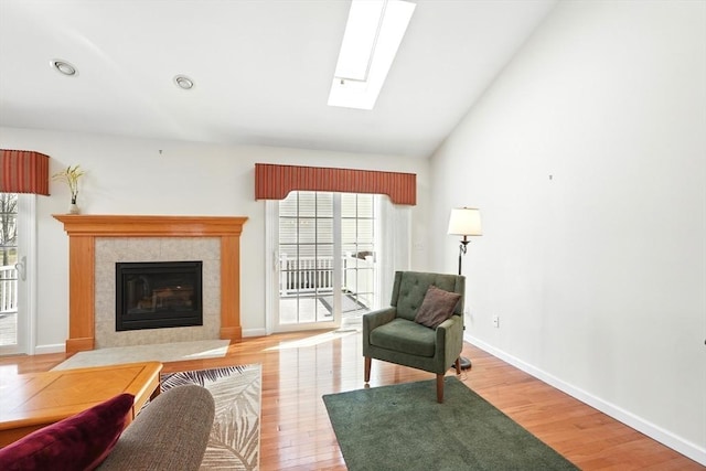 living area with lofted ceiling with skylight, light wood-style floors, baseboards, and a tile fireplace