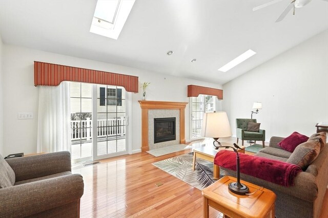 living area featuring visible vents, lofted ceiling with skylight, light wood-type flooring, a tile fireplace, and a ceiling fan