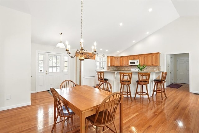 dining room with light wood-type flooring, baseboards, a notable chandelier, and high vaulted ceiling