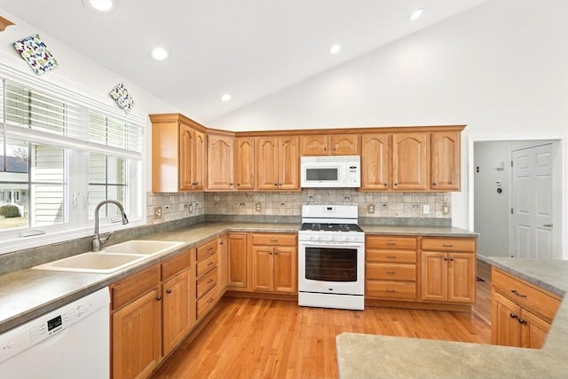 kitchen with white appliances, vaulted ceiling, light wood finished floors, and a sink