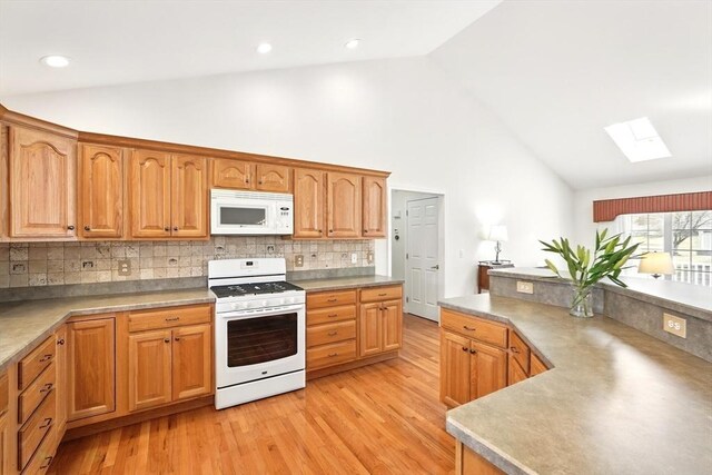 kitchen featuring tasteful backsplash, light wood-type flooring, light countertops, a skylight, and white appliances