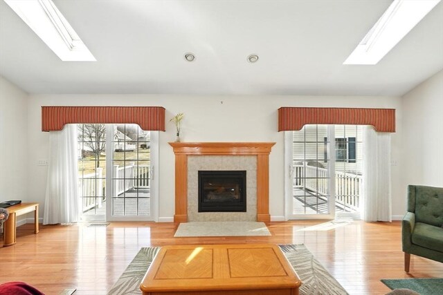 living area with a fireplace, vaulted ceiling with skylight, wood finished floors, and baseboards