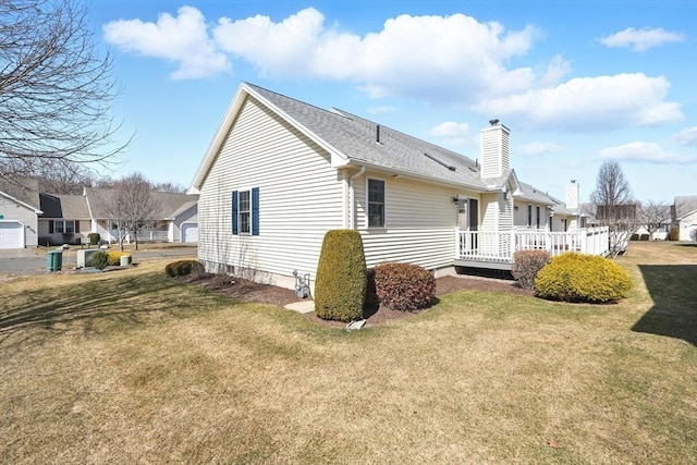 back of house with a yard, roof with shingles, a deck, and a chimney