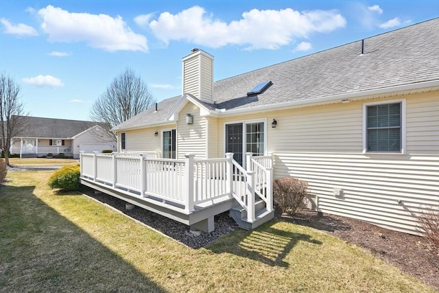 rear view of house featuring a wooden deck, a lawn, roof with shingles, and a chimney